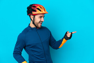 Young cyclist man isolated on blue background pointing finger to the side and presenting a product - obrazy, fototapety, plakaty
