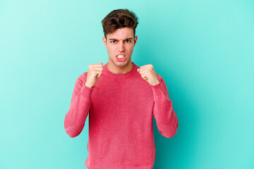 Young caucasian man isolated on blue background upset screaming with tense hands.