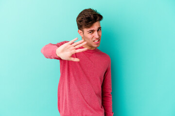 Young caucasian man isolated on blue background rejecting someone showing a gesture of disgust.