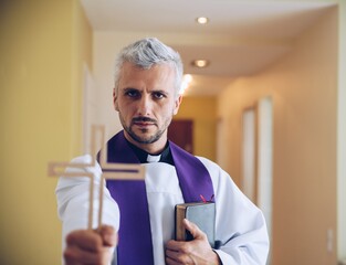 A priest holding a wooden cross in his hand and a Bible in the other hand. Faith symbol.
