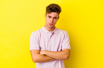 Young caucasian man isolated on yellow background frowning face in displeasure, keeps arms folded.