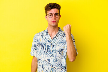 Young caucasian man isolated on yellow background showing fist to camera, aggressive facial expression.