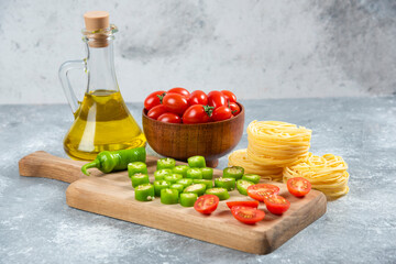 Sliced vegetables, olive oil and pasta nests on marble background