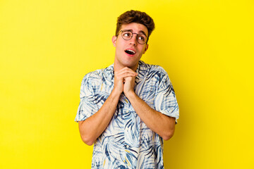 Young caucasian man isolated on yellow background keeps hands under chin, is looking happily aside.