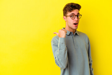 Young caucasian man isolated on yellow background points with thumb finger away, laughing and carefree.