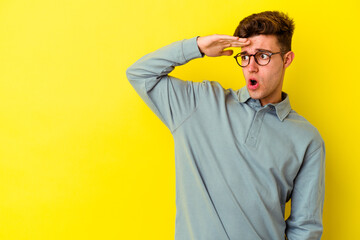 Young caucasian man isolated on yellow background looking far away keeping hand on forehead.