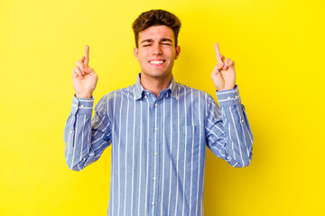 Young caucasian man isolated on yellow background crossing fingers for having luck