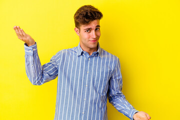 Young caucasian man isolated on yellow background makes scale with arms, feels happy and confident.