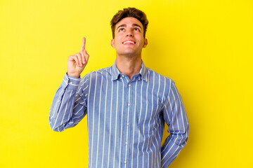 Young caucasian man isolated on yellow background indicates with both fore fingers up showing a...