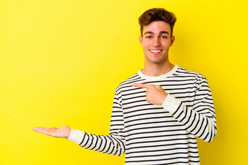 Young caucasian man isolated on yellow background excited holding a copy space on palm.