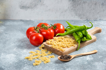 Raw farfalle, tomatoes and chili peppers on wooden board