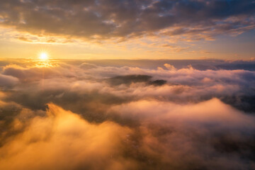 Mountains in clouds at sunrise in summer. Aerial view of mountain peak in fog. Beautiful landscape...