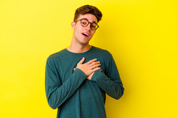 Young caucasian man isolated on yellow background has friendly expression, pressing palm to chest. Love concept.