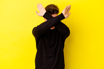 Young caucasian man isolated on yellow background keeping two arms crossed, denial concept.