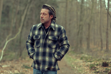 Blonde man in checkered coat on a forest path.