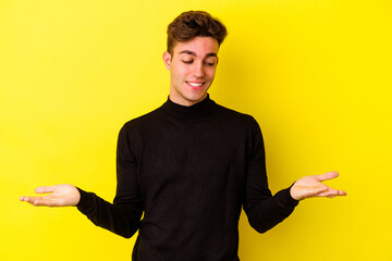 Fototapeta premium Young caucasian man isolated on yellow background holding something with palms, offering to camera.