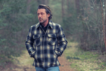 Blonde man in checkered coat walking on a path in a forest.