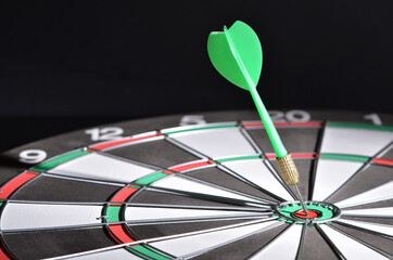 A green dart hitting the bullseye on the dartboard. Selective focus points. Blurred background 