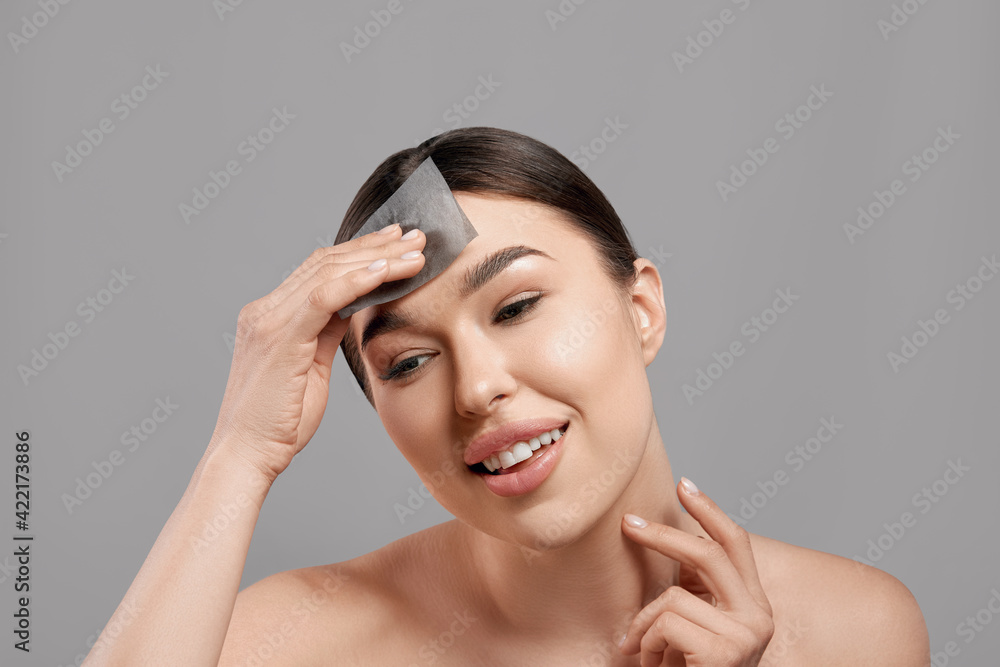 Wall mural skin care. woman removing oil from face using blotting papers. closeup portrait of beautiful healthy