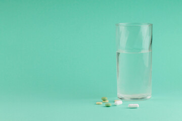 Pills and a glass of water on a green background. 