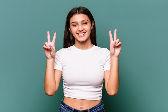 Young Indian woman isolated on blue background showing victory sign and smiling broadly.