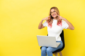 Young woman sitting on a chair with laptop over isolated yellow background giving a thumbs up gesture