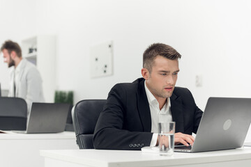 A young purchasing Manager in a black suit makes a large online order via an intranet in a laptop...