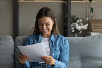 Close up smiling woman reading good news in letter, holding paper sheet in hands, sitting on couch...