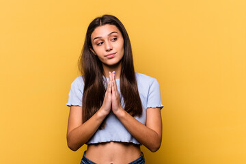 Obraz premium Young Indian woman isolated on yellow background praying, showing devotion, religious person looking for divine inspiration.