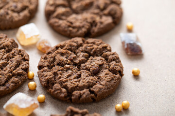 Fragrant chocolate granola cookies with brown cane sugar, spread out on a beige cardboard background. Breakfast cookies close-up