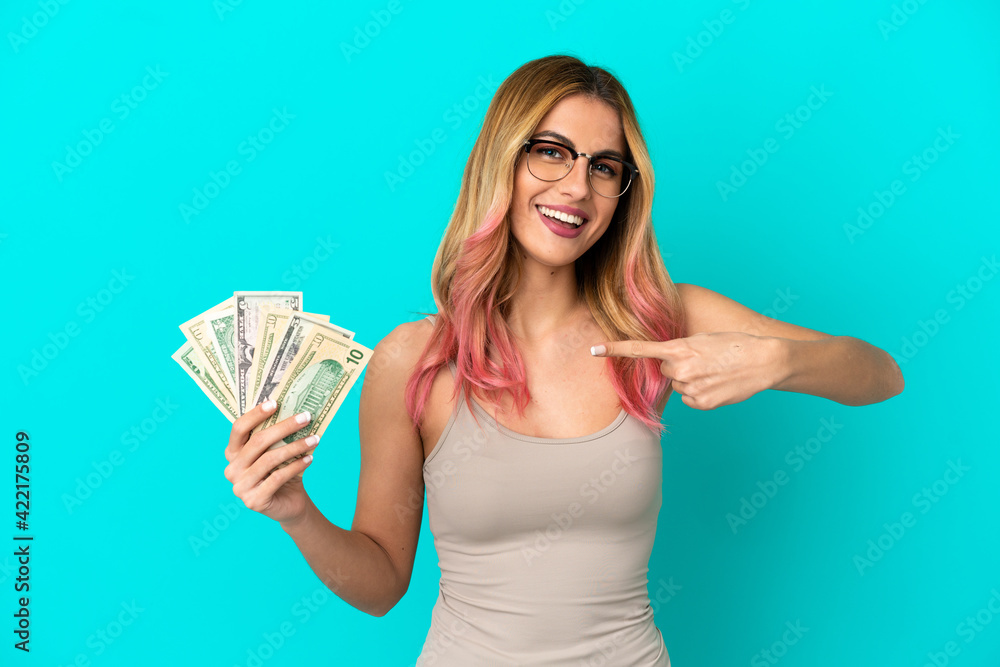 Wall mural young woman taking a lot of money over isolated blue background and pointing it