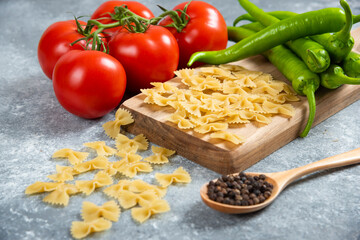 Raw farfalle, tomatoes and chili peppers on wooden board