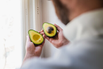 Mani che tengono due metà di un avocado maturo con il nocciolo in vista, illuminate dalla luce...