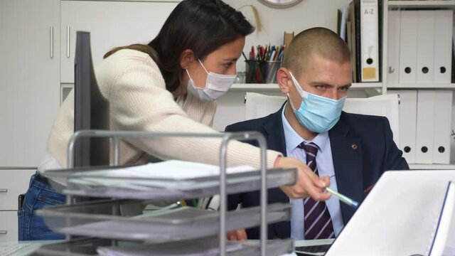  Businessman in protective face mask discussing project with colleague in white modern office