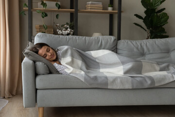 Peaceful attractive woman sleeping under warm blanket plaid on cozy couch at home, enjoying lazy...