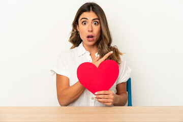 Young caucasian woman holding a valentines day heart isolated pointing to the side