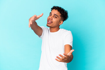 Young african american curly man isolated on blue feels confident giving a hug to the camera.