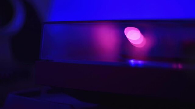 Pan to a record player playing a record while a colorful light flashes, pan, close up.