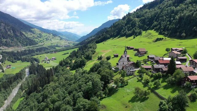 Picturesque aerial view of houses of small Swiss village Cavardiras in mountain valley in sunny summer day. High quality 4k footage