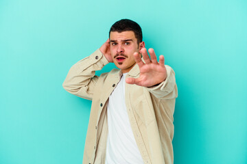 Young caucasian man isolated on blue background being shocked due to an imminent danger