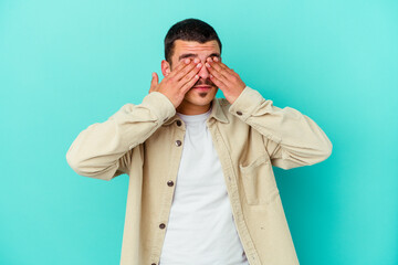 Young caucasian man isolated on blue background afraid covering eyes with hands.