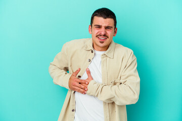 Young caucasian man isolated on blue background having a liver pain, stomach ache.