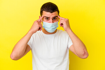 Young caucasian man wearing a protection for coronavirus isolated on yellow background focused on a task, keeping forefingers pointing head.