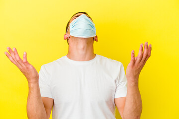 Young caucasian man wearing a protection for coronavirus isolated on yellow background screaming to the sky, looking up, frustrated.