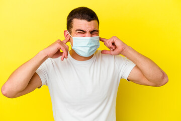 Young caucasian man wearing a protection for coronavirus isolated on yellow background covering...