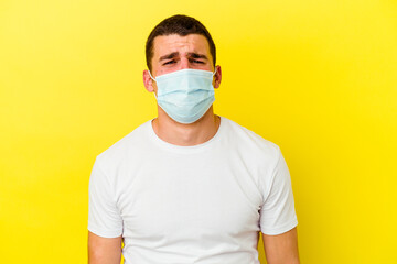 Young caucasian man wearing a protection for coronavirus isolated on yellow background whining and...