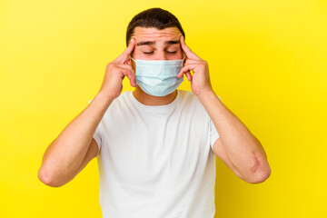 Young caucasian man wearing a protection for coronavirus isolated on yellow background touching temples and having headache.