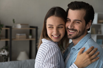 Close up happy young couple family hugging, visualizing good future, looking to aside, standing at...