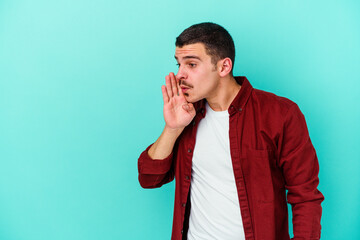 Young caucasian man isolated on blue background is saying a secret hot braking news and looking aside