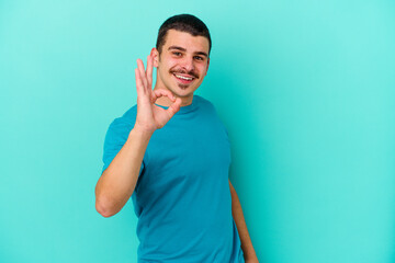 Young caucasian man isolated on blue background cheerful and confident showing ok gesture.